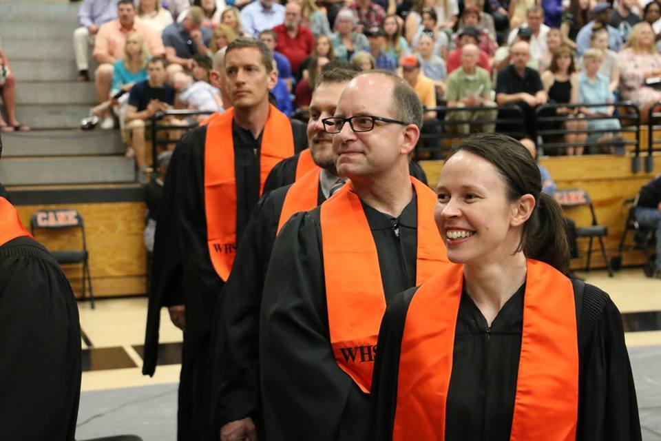 Four teachers at graduation smiling toward stage